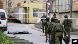 FILE - In this Thursday, March 24, 2016 file photo, Israeli soldiers stand near the body of a Palestinian who was shot and killed by a soldier while laying wounded on the ground after a stabbing attack in Hebron, West Bank. 