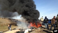 在美国北达科他州，抗议在“达科他输油管线”铺设管道的人焚烧垃圾，而警察以及国民警卫队官员穿过燃烧着的障碍物，缓慢包围抗议者的营地（2016年10月27日）
