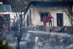 Para migran mengamati petugas pemadam kebakaran yang tengah menyemprotkan air untuk memadamkan sisa-sisa api kebakaran di dalam kamp pengungsi dan migran di pulau Samos, Yunani, Senin, 2 November 2020.