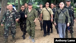 President Rodrigo Duterte, center left, wearing a cap and an assault rifle slung on his shoulder, walks with other military officers and security men inside the camp of the 2nd Mechanized Infantry Brigade, Light Armored Division, July 7, 2017, in the outskirts of Iligan city in southern Philippines. 