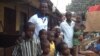 Daddy Hasan Kamara stands outside his Freetown, Sierra Leone, home with family members.