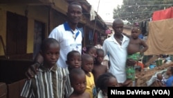 Daddy Hasan Kamara stands outside his Freetown, Sierra Leone, home with family members.