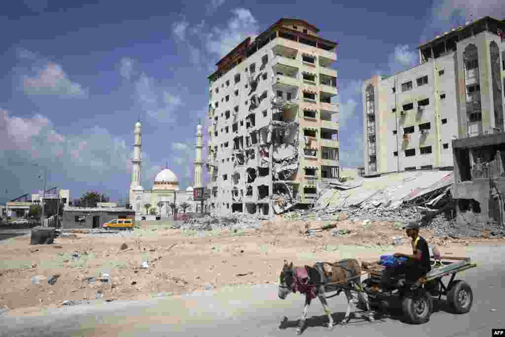 A Palestinian man rides his donkey cart past a building that was destroyed during the 11-day war in May of this year between Israel and the Palestinian Hamas movement, in Gaza City.