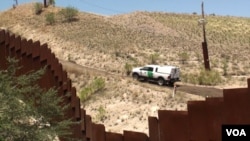 The view from the Mexican side as a US Border Patrol car passes a fence. (G. Flakus/VOA)