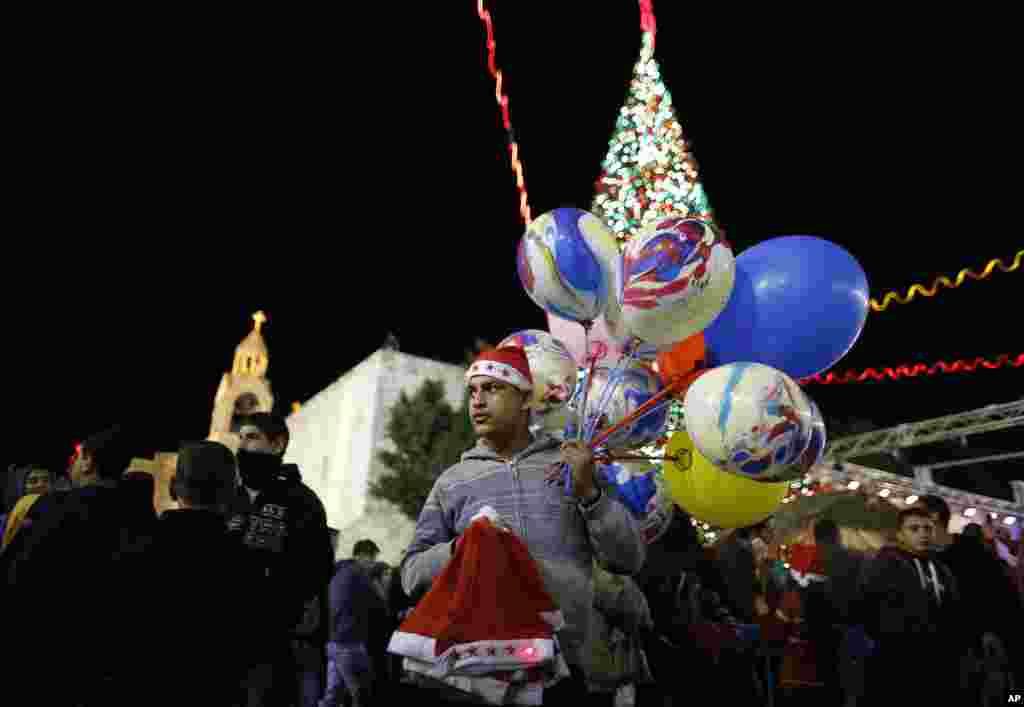 Pedagang Palestina menjual balon dan topi Natal di Alun-Alun Manger, di luar Gereja Nativity (24/12).