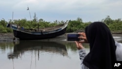 FILE - An Acehnese woman uses her mobile phone to take pictures of the boat carrying a group of ethnic-Rohingya that was brought ashore in Bireuen, Aceh province, Indonesia, April 20, 2018. 