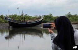 FILE - An Acehnese woman uses her mobile phone to take pictures of the boat carrying a group of ethnic-Rohingya that was brought ashore in Bireuen, Aceh province, Indonesia, April 20, 2018.