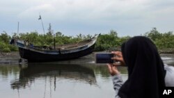 FILE - An Acehnese woman uses her cell phone to take a picture of a boat that carried a group of ethnic Rohingya after it washed ashore in Bireuen, Aceh province, Indonesia, April 20, 2018. 