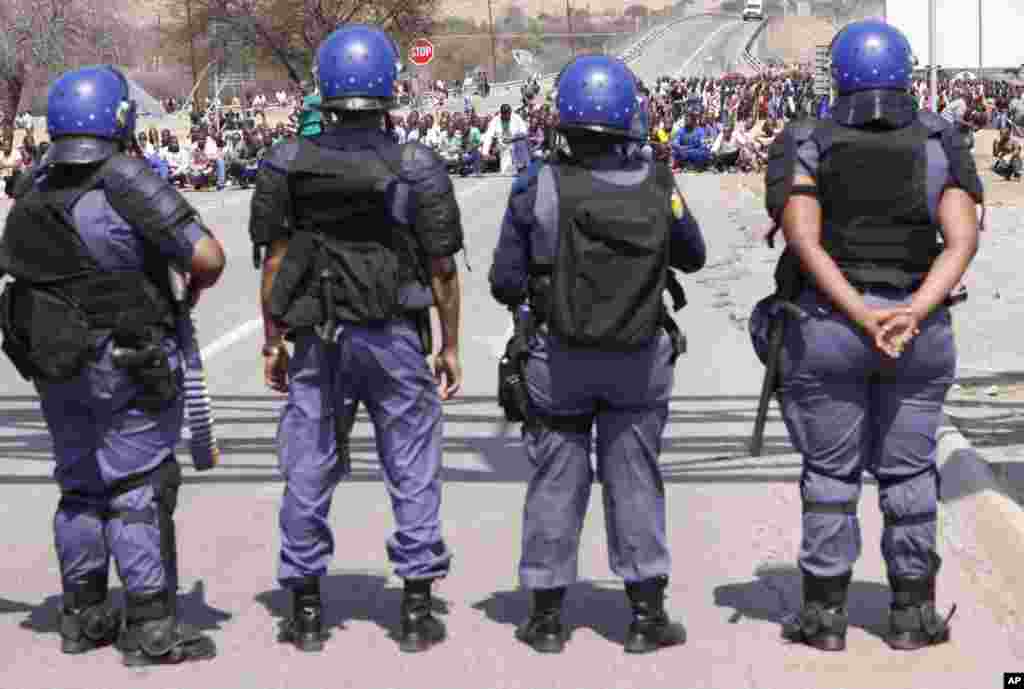 Police keep an eye on striking mine workers as they march to a smelter plant at the Lonmin Platinum Mine near Rustenburg, South Africa, September, 12, 2012.