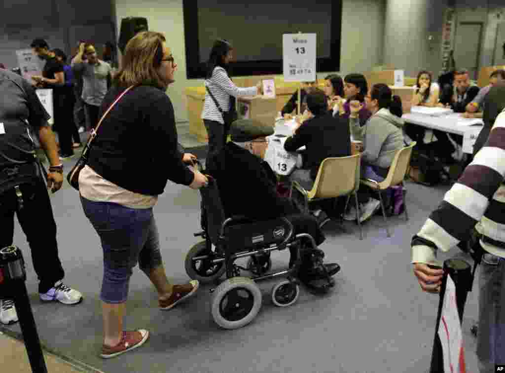 Seorang perempuan Venezuela membantu seorang pria yang memiliki disabilitas di dalam tempat pemungutan suara untuk warga Venezuela yang ada di Madrid, Spanyol (14/4). (AP/Andres Kudacki)