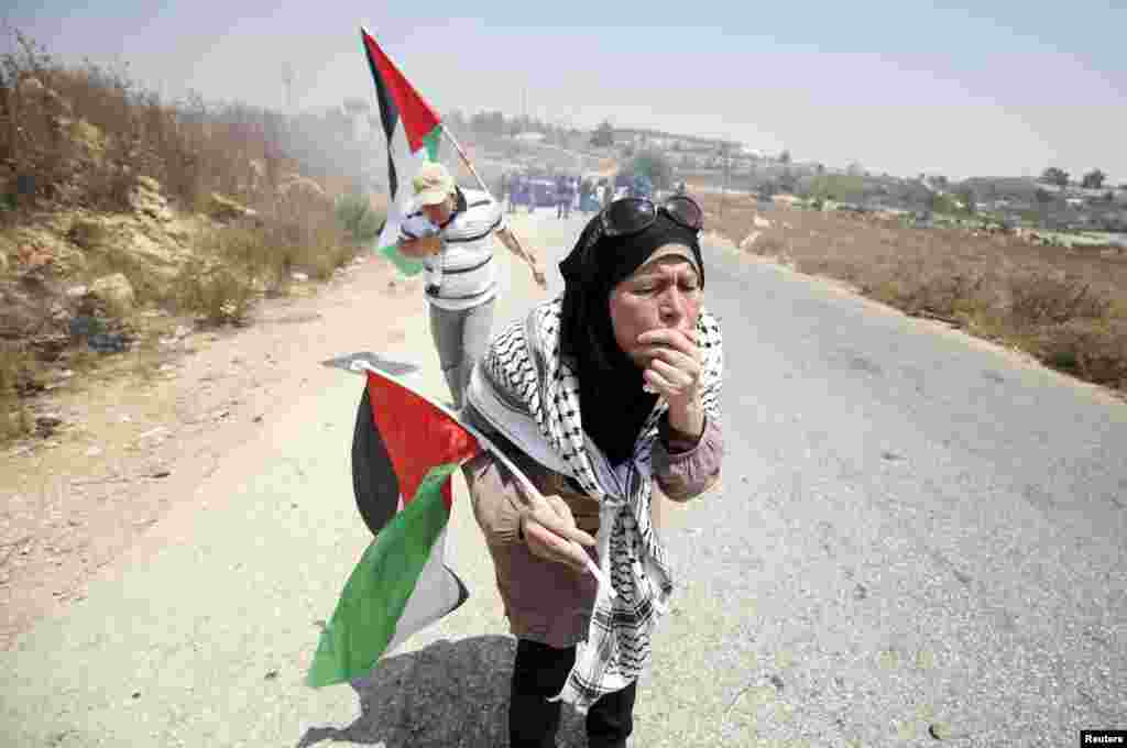 Palestinian protesters holding Palestinian flags react to tear gas fired by Israeli troops during clashes at a protest against Jewish settlements in the West Bank village of Nabi Saleh, near Ramallah.