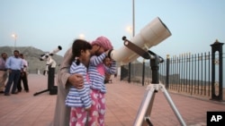 Seorang bapak memeluk anak perempuannya sambil melihat teropong untuk melihat posisi bulan di puncak gunung Jebel Hafeet sebelum bulan suci Ramadan, di Al Ain, Uni Emirat Arab, 16 Juni 2015.
