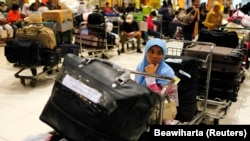 Seorang tenaga kerja perempuan Indonesia duduk di atas troli ketika menunggu berkas miliknya diperiksa saat tiba di Bandara Soekarno-Hatta. (Foto dok: Reuters/Beawiharta)