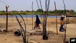 FILE - Chadian women walk past destroyed homes, in the Lake Chad shore village of N'Gouboua. Guerrillas have recently ramped up attacks in remote border areas around Lake Chad.