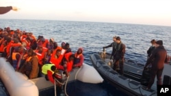 In this March 2014 photo released by the Italian Navy, migrants stand on after being rescued along the Mediterranean sea.