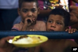 In this March 8, 2018 photo, Venezuelan children wait for a free meal at a migrant shelter set up at the Tancredo Neves Gymnasium in Boa Vista, Roraima state, Brazil.