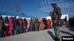 Voters line up to cast their votes as an Indian security officer stands guard outside a polling station during the last phase of the Jammu and Kashmir state assembly elections on the outskirts of Jammu, Dec. 20, 2014.