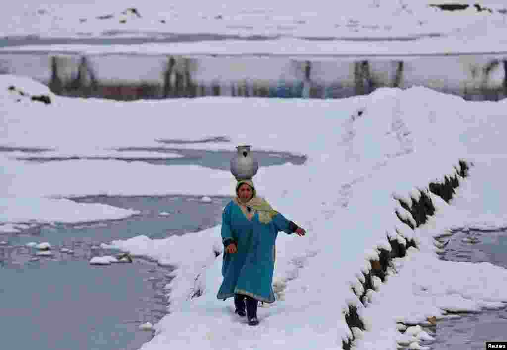 Seorang perempuan membawa kendi air berjalan melalui sebuah lapangan yang tertutup salju di pinggiran Srinagar, Kashmir-India.&nbsp;(Foto: Reuters)