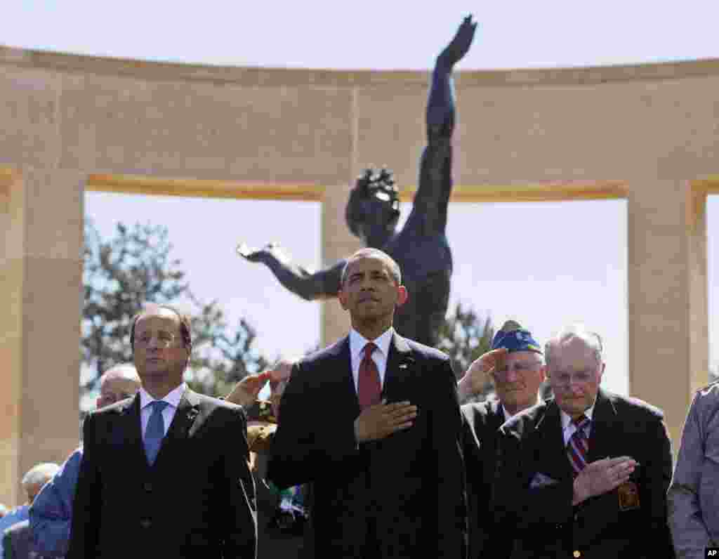 U.S. President Barack Obama and French President Francois Hollande stand with veterans during the playing of Taps, at Normandy American Cemetery at Omaha Beach in Colleville sur Mer, Normandy, France, June 6, 2014. 