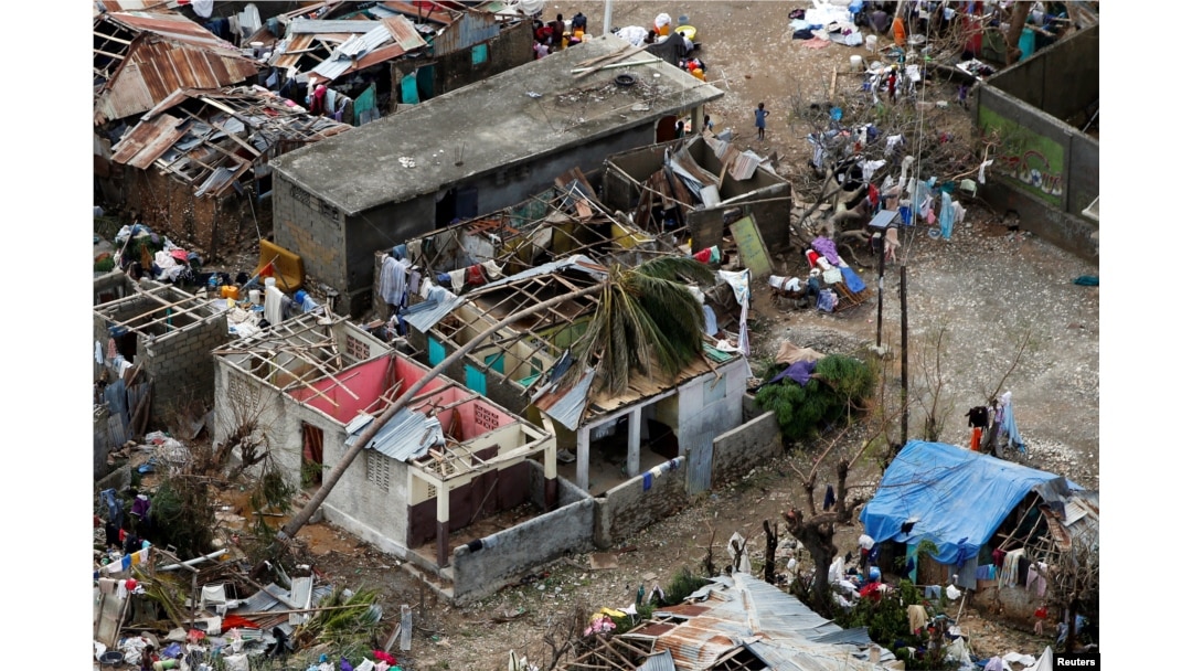 FILE- People stand next to destroyed houses after Hurricane Matthew passed Jeremie, Haiti, Oct. 6, 2016.