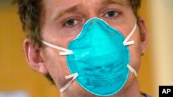 Registered nurse Scott McGieson wears an N95 mask as he walks out of a patient's room in the acute care unit of Harborview Medical Center, Jan. 14, 2022, in Seattle. 