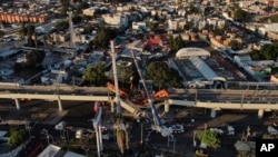 An aerial view of subway cars dangle at an angle from a collapsed elevated section of the metro, in Mexico City, Tuesday, May 4, 2021. 