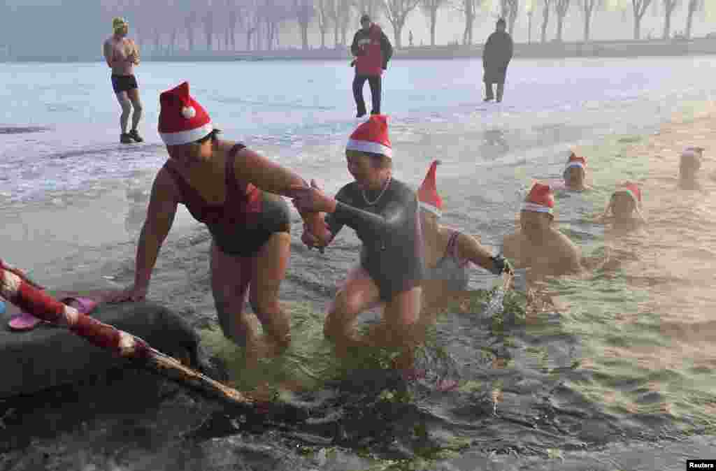 Para perenang musim dingin yang memakai topi Sinterklas muncul dari danau yang setengah beku setelah berenang di air sedingin es untuk merayakan Natal di sebuah taman di Shenyang, provinsi Liaoning (24/12).