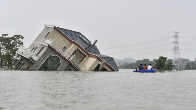 中国江西省上饶市鄱阳湖附近地区被洪水淹没，几人划着小船经过一所被洪水冲倒的民宅。（2020年7月15日）
