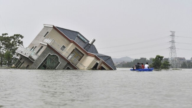 中国江西省上饶市鄱阳湖附近地区被洪水淹没,几人划着小船经过一所被洪水冲倒的民宅。(2020年7月15日)