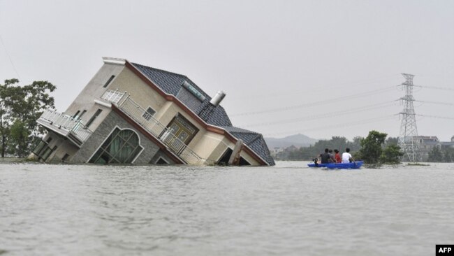 中国江西省上饶市鄱阳湖附近地区被洪水淹没,一人划着小船经过一所被洪水冲倒的民宅。(2020年7月15日)