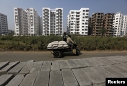 FILE- Laborers transport cement bags onto an improvised motorized rickshaw at the construction site of a residential complex on the outskirts of Kolkata, India, Jan. 23, 2016.
