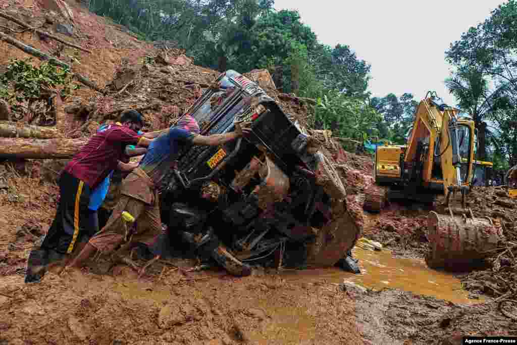 Rescue workers push a overturned vehicle stuck in the mud and debris at a site of a landslide caused by heavy rains in Kokkayar in India&#39;s Kerala state.