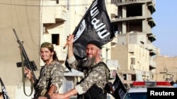 FILE - Fighters with the militant group Islamic State in Iraq and the Levant (ISIL, also called ISIS by some) wave flags as they take part in a military parade along the streets of Raqqa province, northern Syria, June 30, 2014. 