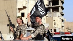 Fighters with the militant group Islamic State wave flags as they hold a military parade along the streets of Raqqa in northern Syria, June 30, 2014. 