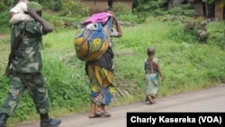 Un soldat, kalachnikov en bandoulière, un enfant sur ses épaules, marche derrière une femme et un enfant près d’un camp de déplacés à OICHA, dans le Nord-Kivu. VOA/Charly Kasereka