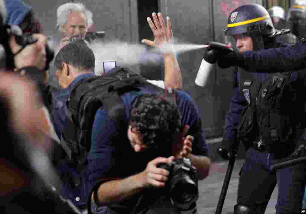 Riot police officers spray gas at photographers during scuffles part of a demonstration in Paris, France. Public services workers have gone on strike as part of their protest a government plan to cut 120,000 jobs by 2022.