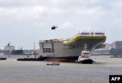 Kapal tunda memandu kapal induk buatan dalam negeri INS Vikrant saat meninggalkan dermaga Cochin Shipyard Limited setelah diluncurkan di Kochi. (Foto: AFP)