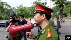 FILE - A Vietnamese police officer uses a speaker to order pedestrians including journalists to leave a closed area near the Chinese Embassy in Hanoi, Vietnam. 