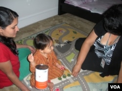 With Vijan's mother Bhawana looking on, family support worker Tina Fontaine uses play time to help develop the baby's motor skills. (VOA/J. Taboh)