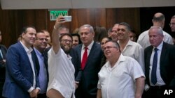 Knesset member Oren Hazan takes a selfie with Israel's Prime Minister Benjamin Netanyahu, center, and MP David Bitan, right of Netanyahu, after a Knesset session that passed of a contentious bill, in Jerusalem, Thursday, July 19, 2018. Israel's parliament approved a controversial piece of legislation early Thursday that defines the country as the nation-state of the Jewish people. Opponents and rights groups have criticized the legislation, warning that it will sideline minorities such as the country's Arabs.