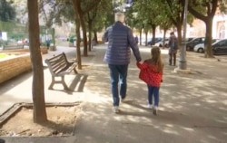 Seorang anak berjalan bersama kakek neneknya di sepanjang jalan dengan deretan pohon di Roma, Italia, Kamis 5 Maret 2020. (Foto: AP)