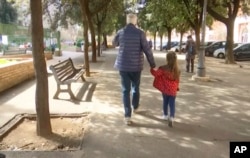 A young girl walks with her elderly grandparent along a tree-lined street in Rome, Italy, March 5, 2020. (AP Photo)