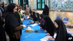 Iranian voters, left, arrive at a polling station to vote for their country's parliamentary and Experts Assembly elections as election staff receive them in Tehran, Iran, Feb. 26, 2016. 
