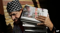 An Egyptian carries a load of newspapers fronted by pictures of clashes following the verdict in the trial of ousted President Hosni Mubarak in Cairo, Egypt, Dec. 1, 2014. 