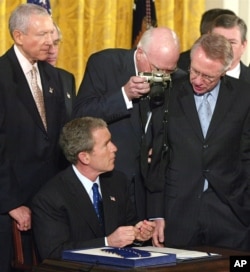 FILE - Sen Patrick Leahy, D-Vt., peers over the shoulder with his camera as President George W. Bush signs Patriot Act legislation during a ceremony in the White House East Room, Oct. 26, 2001.