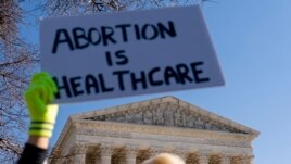 A woman in an doctors clothing holds a sign that reads 