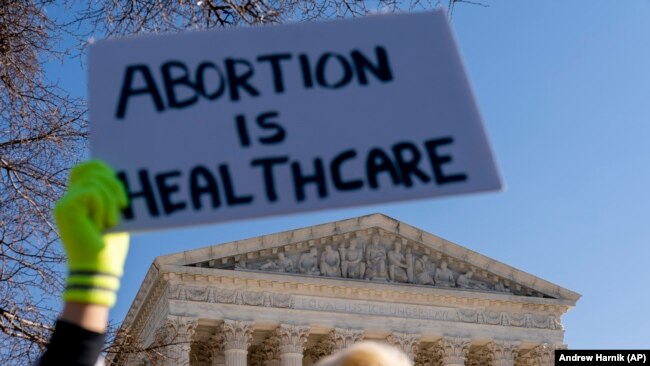 A woman in an doctors clothing holds a sign that reads "Abortion is Healthcare" as abortion rights supporters and anti-abortion protesters demonstrate in front of the U.S. Supreme Court on December 1, 2021, in Washington, as the court hears arguments in a case from Mississippi. A 2018 law would ban abortions after 15 weeks of pregnancy. (AP Photo/Andrew Harnik)