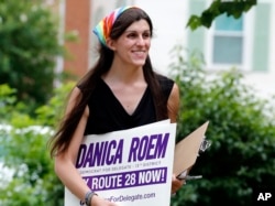 FILE - Danica Roem, then the Democratic nominee for the House of Delegates 13th district seat, holds campaign signs as she canvasses in Manassas, Va., June 21, 2017. Roem became the first openly transgender woman elected to a state legislature when she de