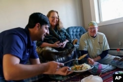 Ihsanullah Patan, left, a horticulturist and refugee from Afghanistan, has lunch with Caroline Clarin, right, whom he worked with in Afghanistan, and her wife, Sheril Raymond, at his home in Fergus Falls, Minn., Oct. 29, 2021.