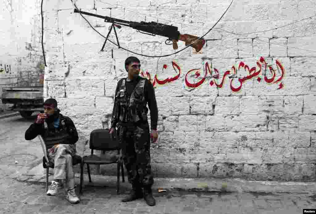 Free Syrian Army fighters rest in front of a graffiti that reads 'Surely your Lord's assault is strict indeed' in the old city of Aleppo, Jan. 22, 2014.